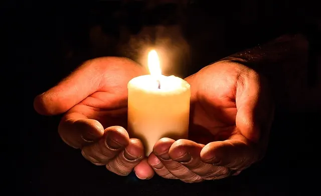 Dos manos ahuecadas sostienen una vela encendida en la oscuridad