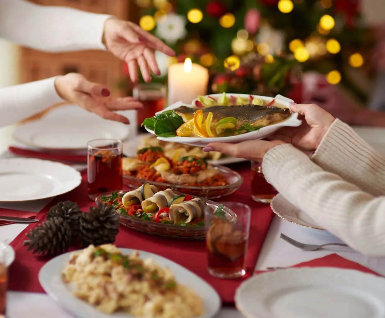 Manos sirviendo platos de entrantes en una mesa de Nochebuena con velas