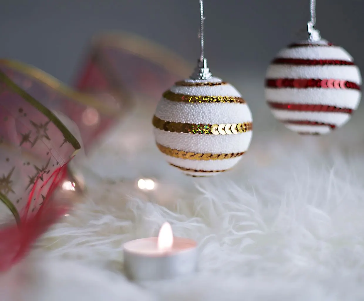 Dos bolas de Navidad de rayas blancas, rojas y doradas junto a una vela encendida