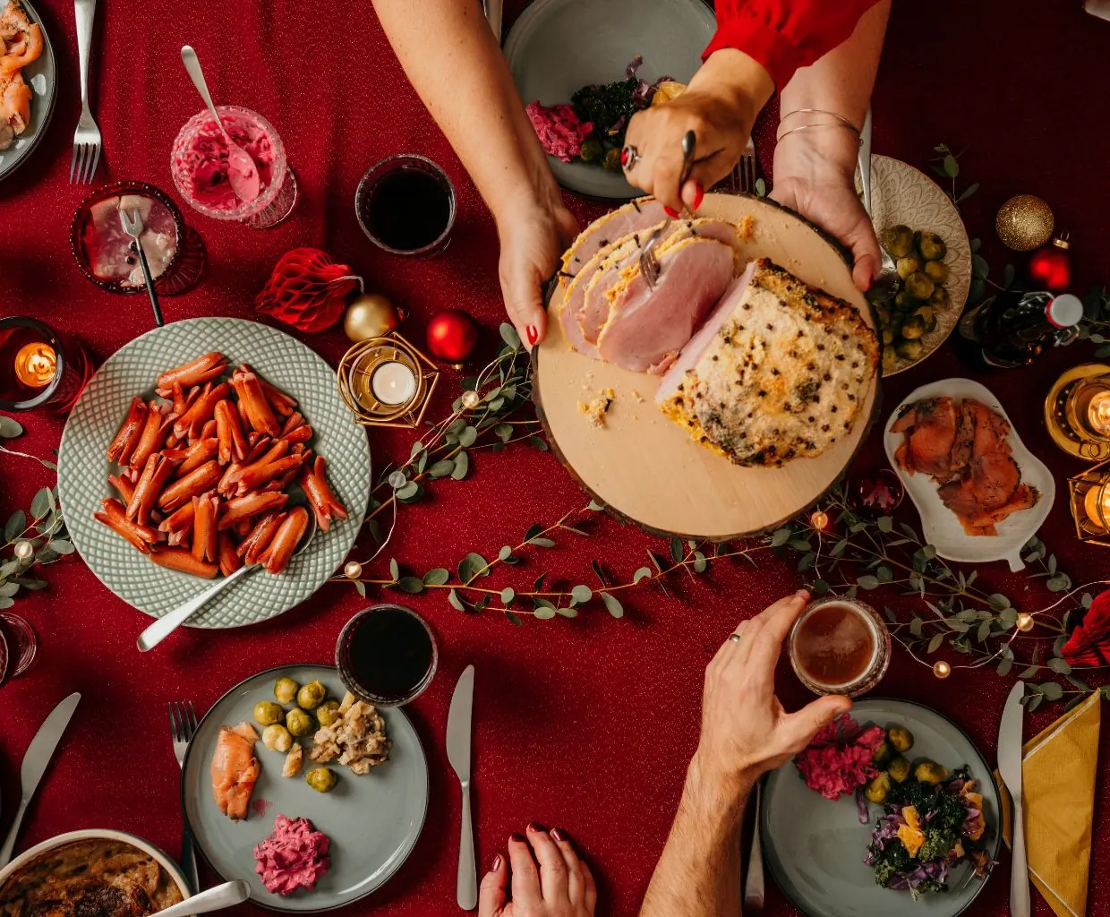 Vista cenital de una mesa de Navidad con varios platos de comida y manos sirviendo