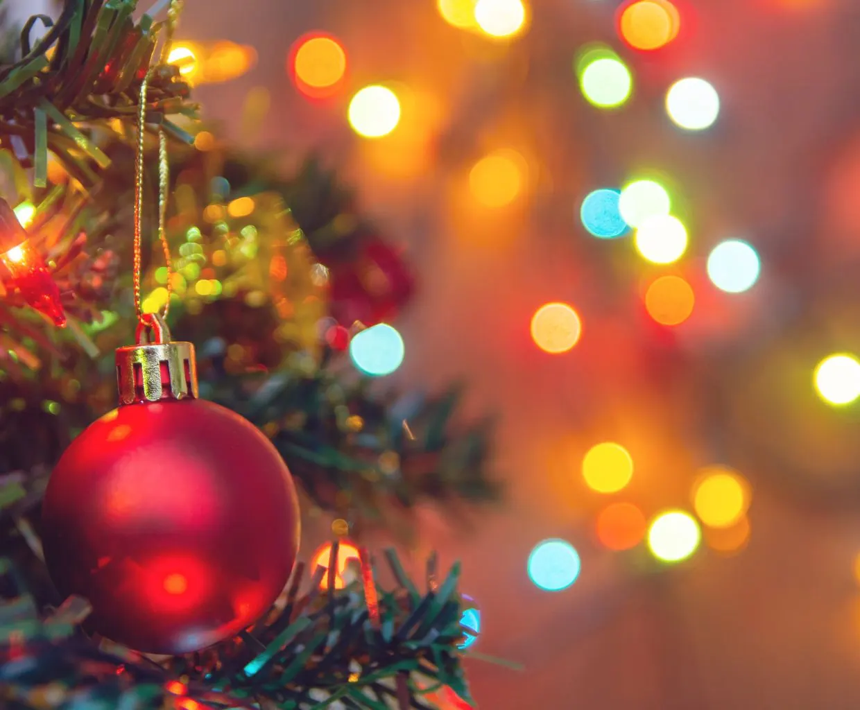 Bola de Navidad roja colgada en un árbol con luces desenfocadas