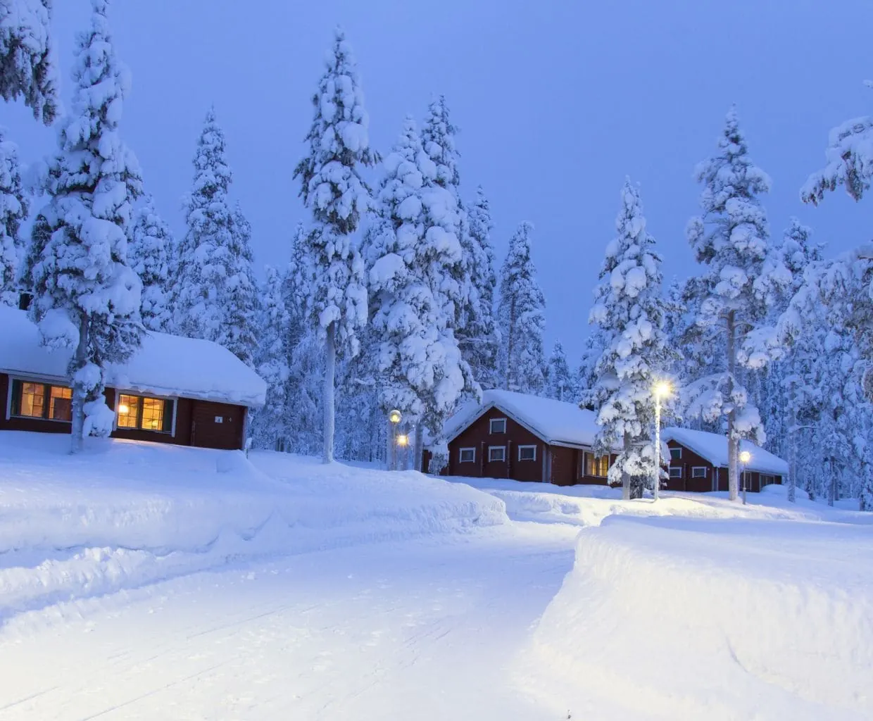 Cabañas nevadas entre abetos cubiertos de nieve al anochecer