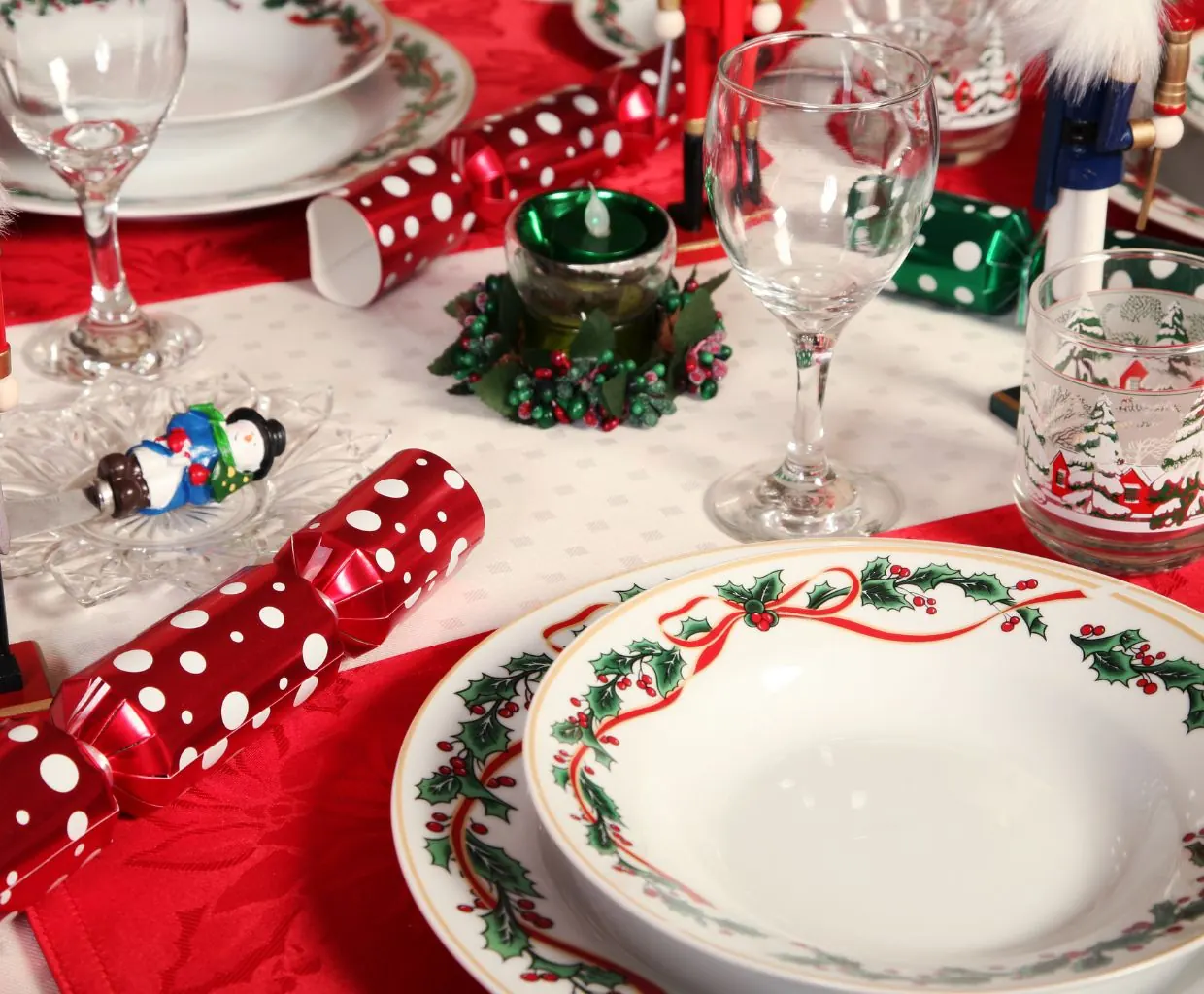 Mesa de Navidad con mantel blanco, platos con motivos navideños, copas y detalles en rojo