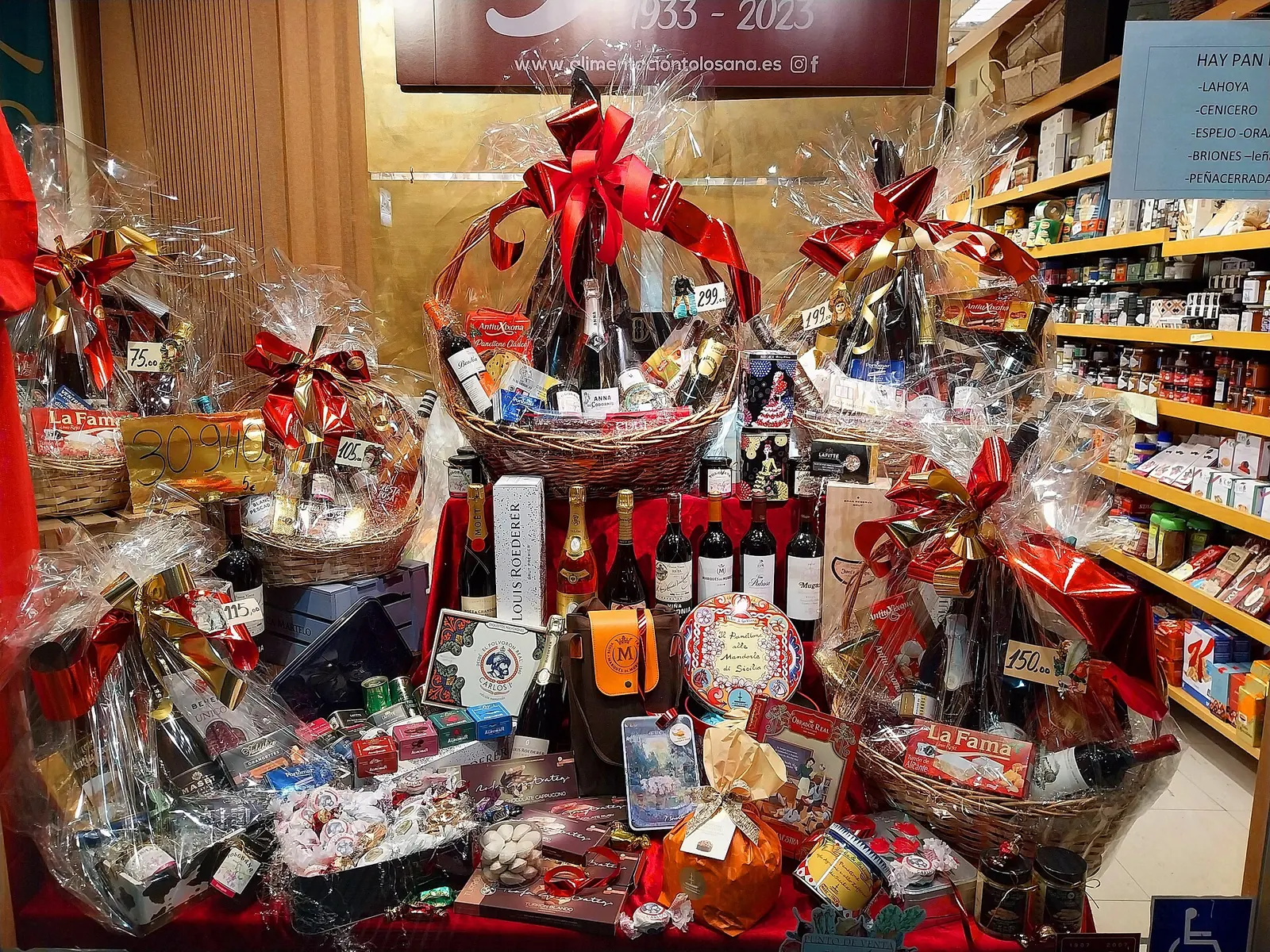 Escaparate con cestas de Navidad envueltas en celofán y lazos rojos, llenas de vinos, cava y dulces