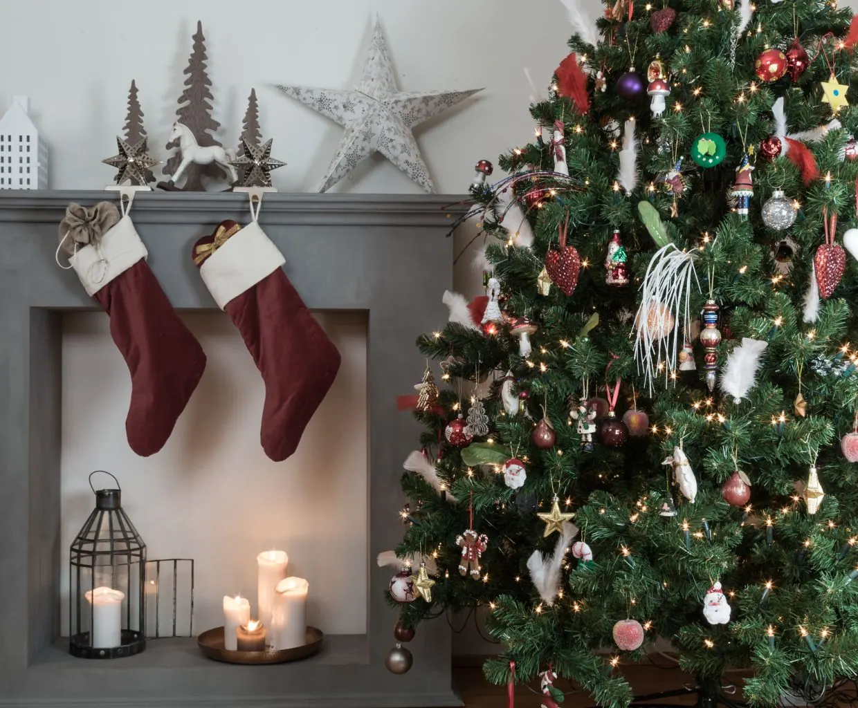 Rincón acogedor con árbol de Navidad decorado e iluminado junto a una chimenea con calcetines colgados y faroles