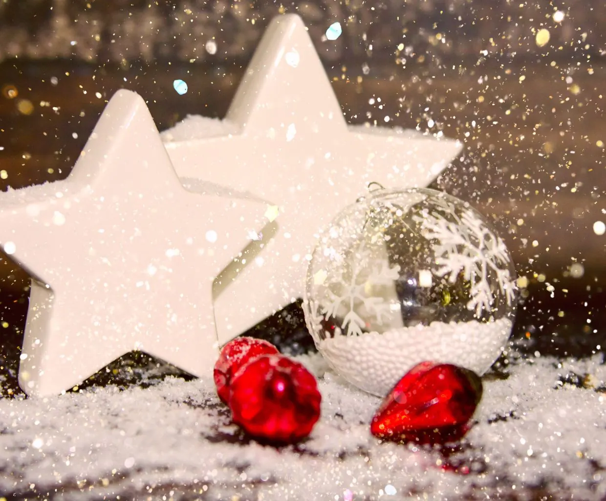 Estrellas blancas de madera sobre nieve artificial con bolas rojas de Navidad