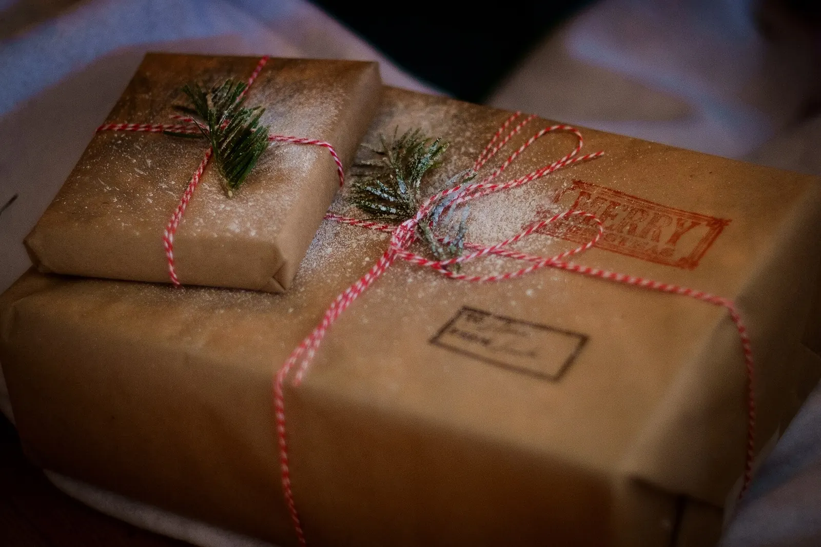 Regalos envueltos en papel kraft con cordel rojo y blanco, ramitas de abeto y un sello de Merry Christmas
