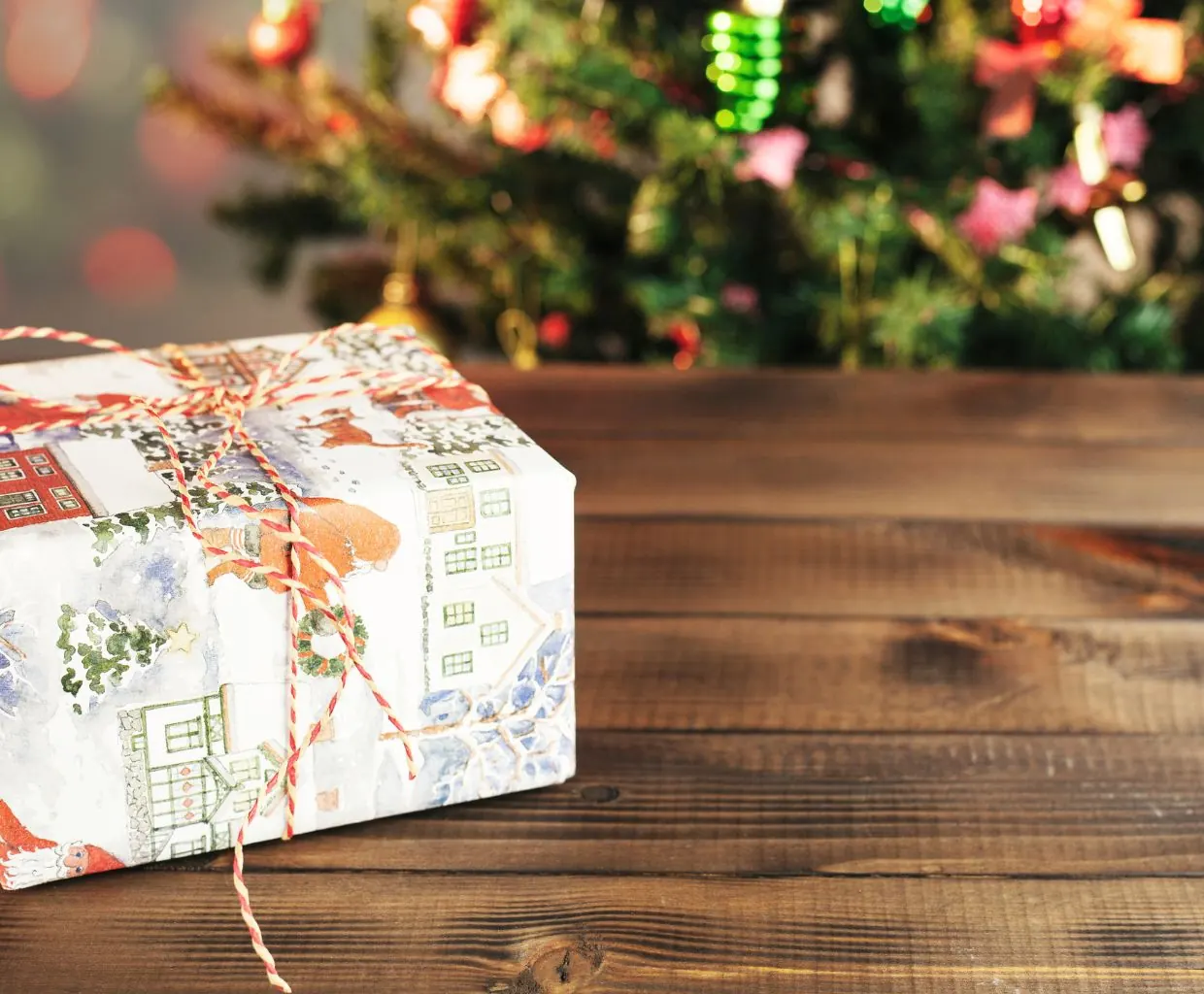 Regalo envuelto con lazo rojo sobre una mesa de madera rústica bajo un árbol de Navidad decorado