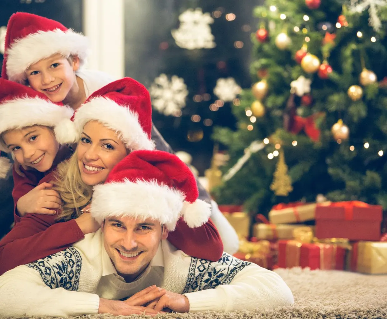 Familia sonriente con gorros rojos de Papá Noel junto al árbol de Navidad