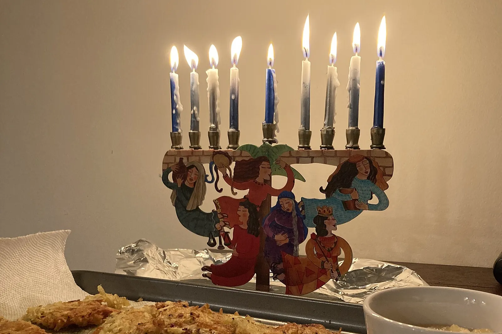 Janukiá con nueve velas azules y blancas encendidas junto a un plato de latkes y compota de manzana