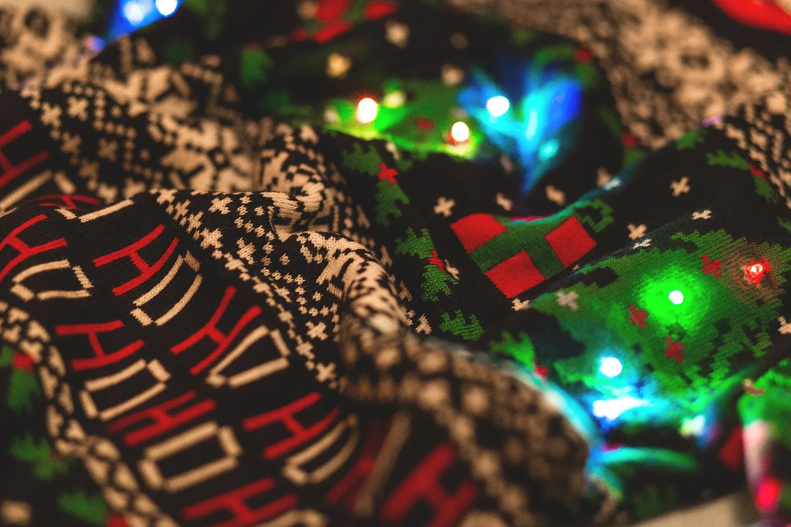 Jersey navideño de punto con motivos de copos, abetos y la palabra HO HO HO, junto a luces de colores