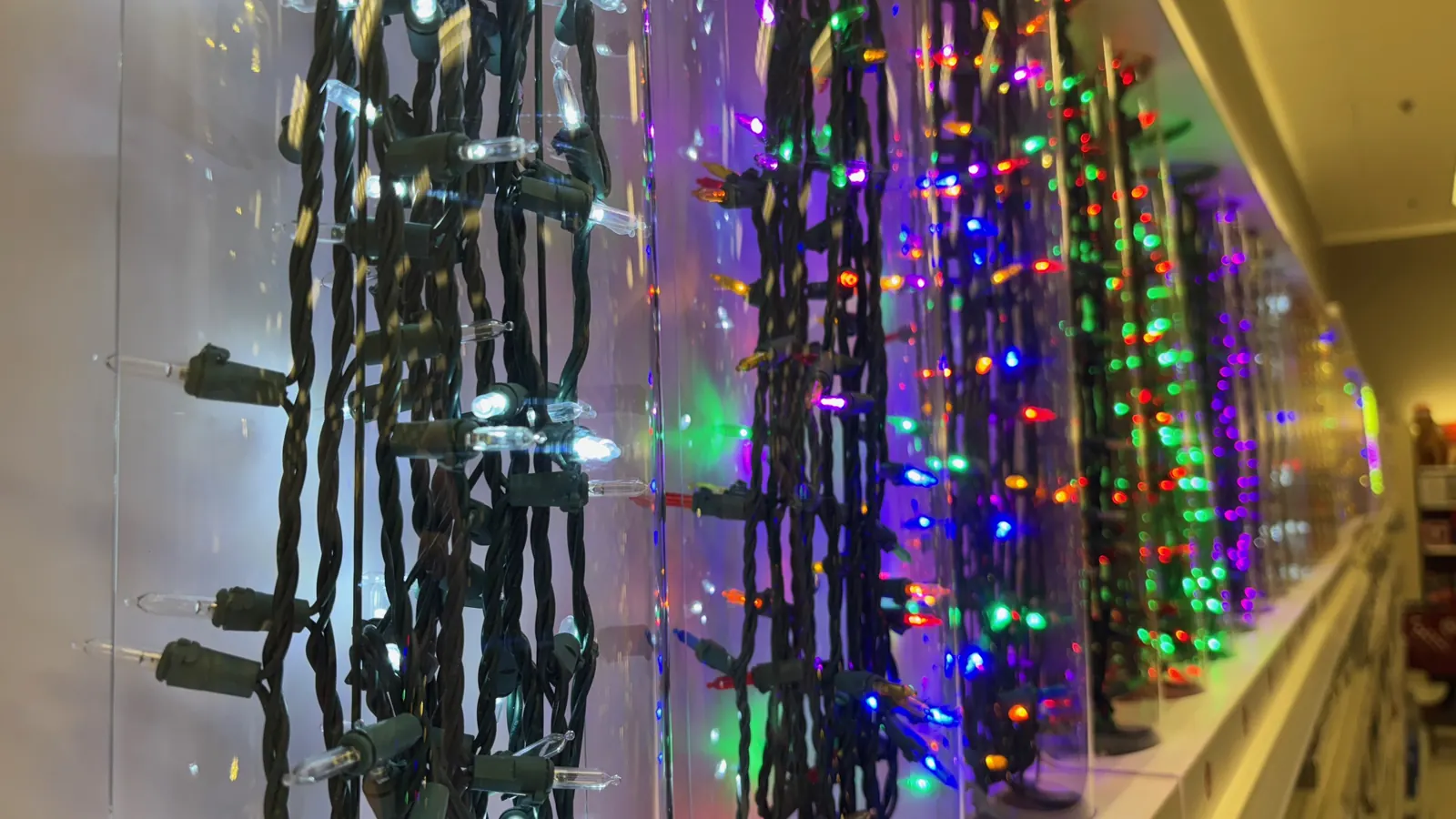 Tiras de luces de Navidad de colores encendidas, colgadas en fila en una tienda