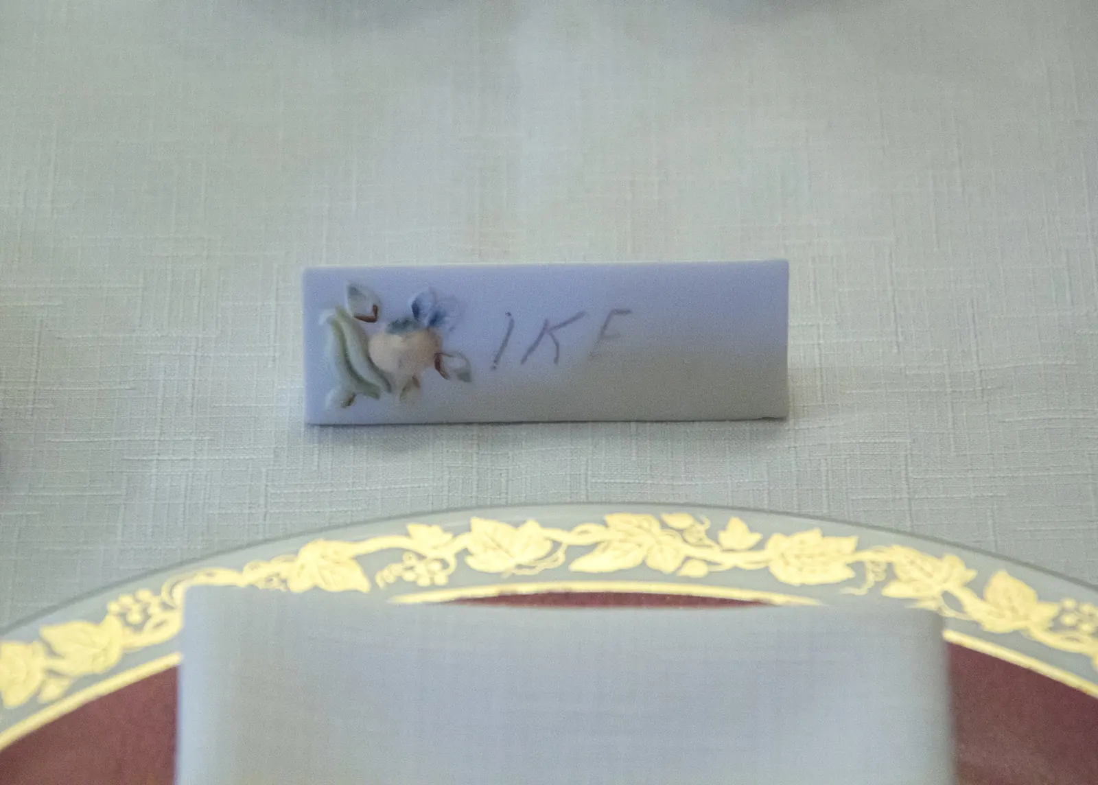 Mesa de comedor larga con mantel blanco hasta casi el suelo, vajilla roja, sillas tapizadas y flores de Pascua al fondo