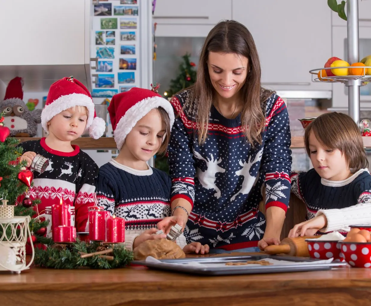 Madre e hijos con jerséis navideños sentados a la mesa de la cocina decorando galletas de Navidad