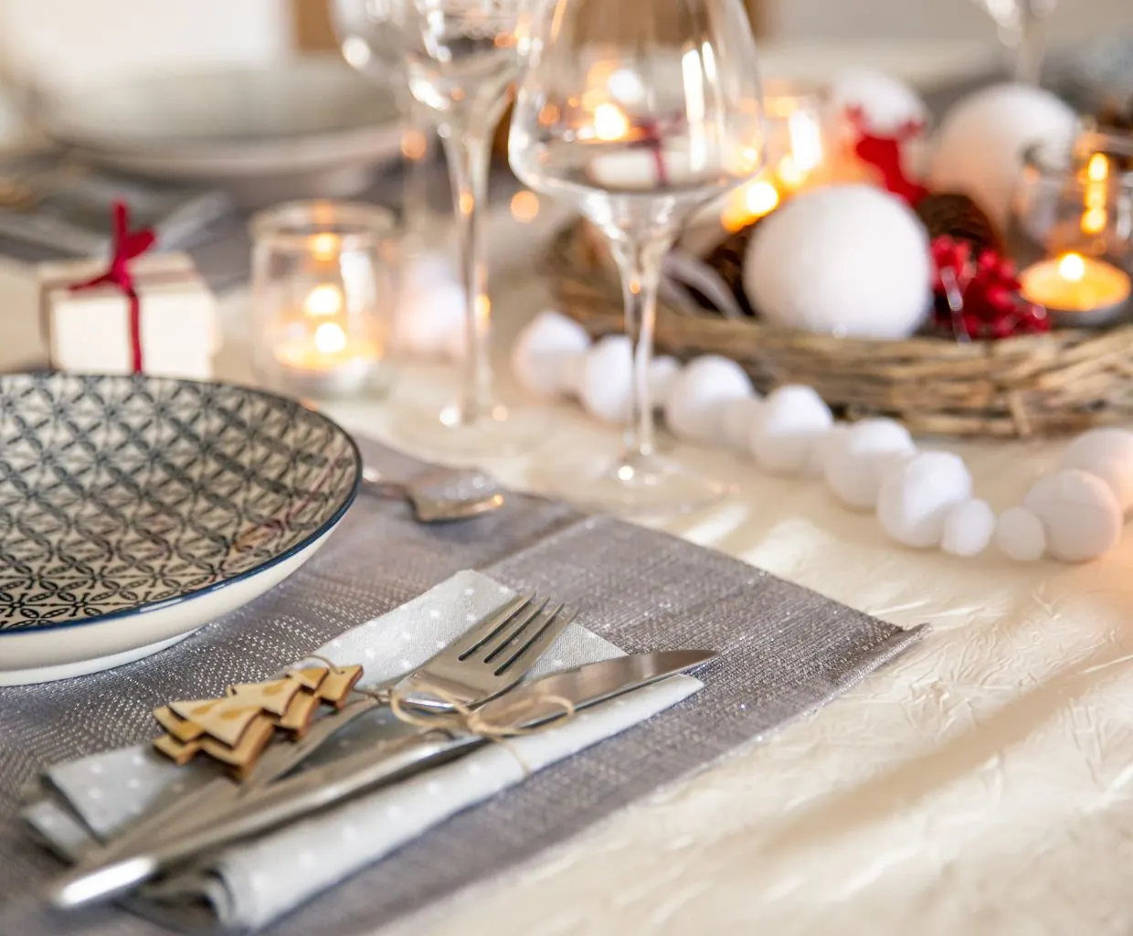 Mesa de Navidad elegante con platos blancos, servilleta de lino, pequeños adornos dorados, copas de vino y velas encendidas