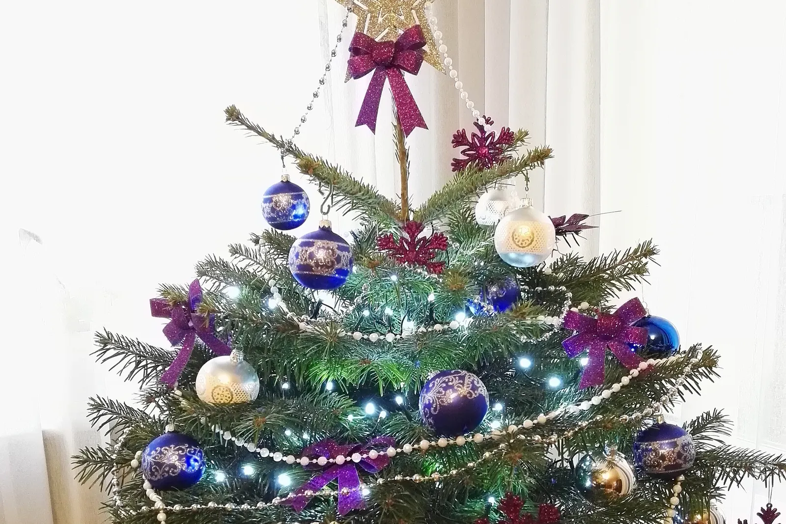 Abeto natural plantado en maceta y decorado con bolas, lazos y luces, sobre una mesita junto a la ventana