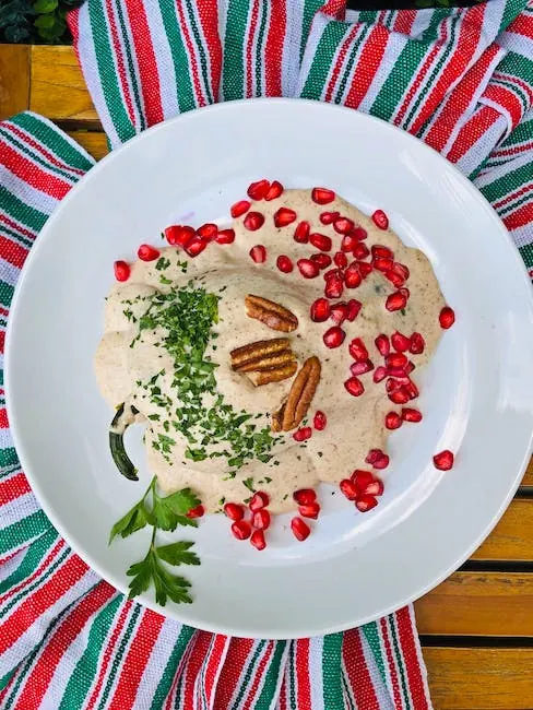 Plato adornado con granada y perejil sobre un mantel navideño de rayas rojas, blancas y verdes