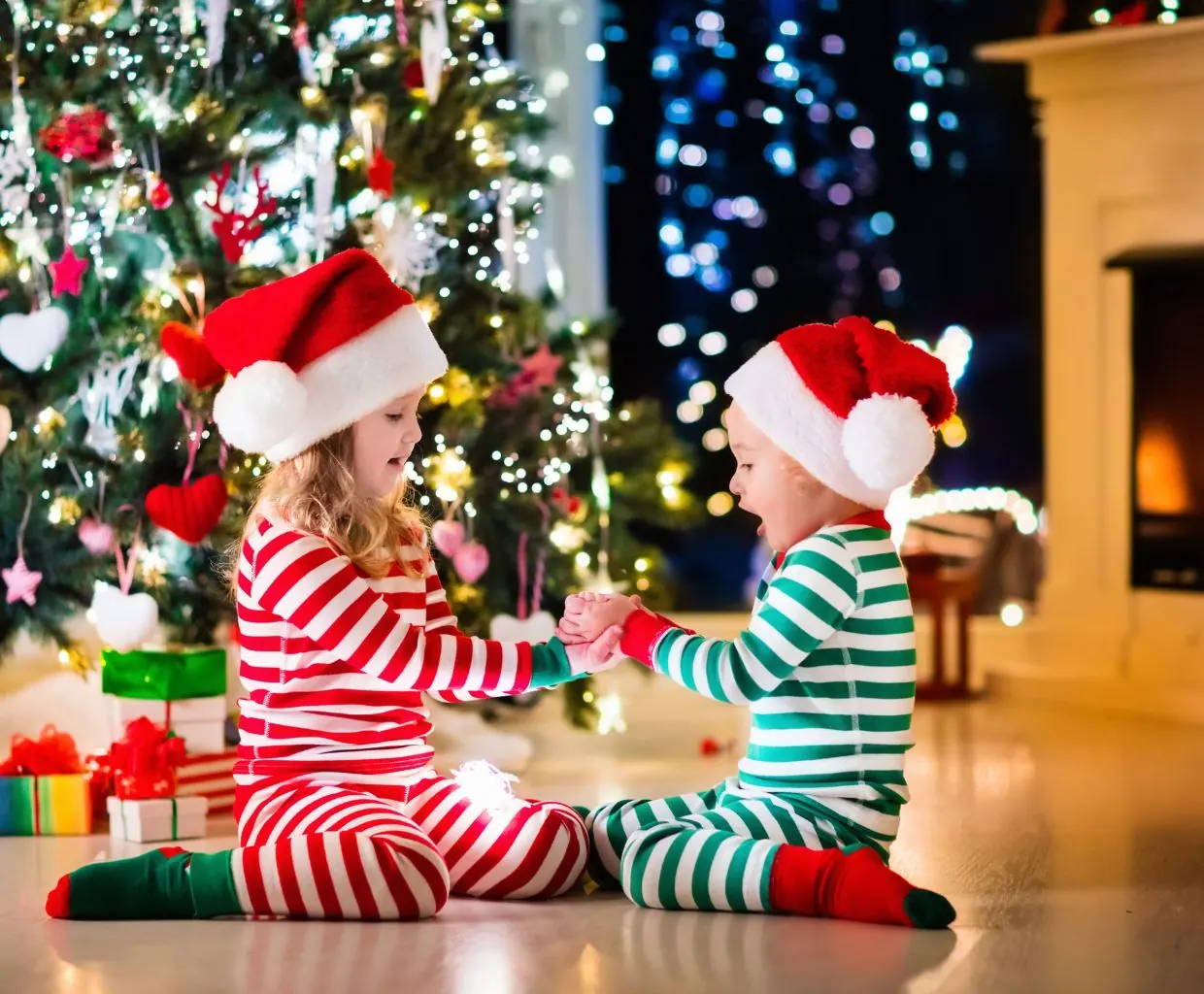 Dos niños con pijamas navideños de rayas jugando junto al árbol de Navidad