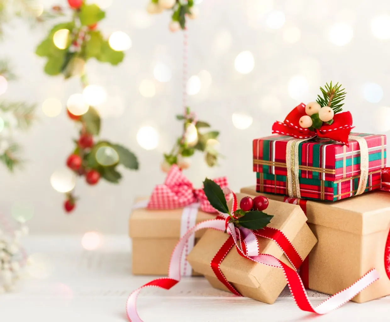 Cajas de regalo envueltas en papel blanco y rojo con lazos rojos y una ramita de acebo sobre fondo blanco