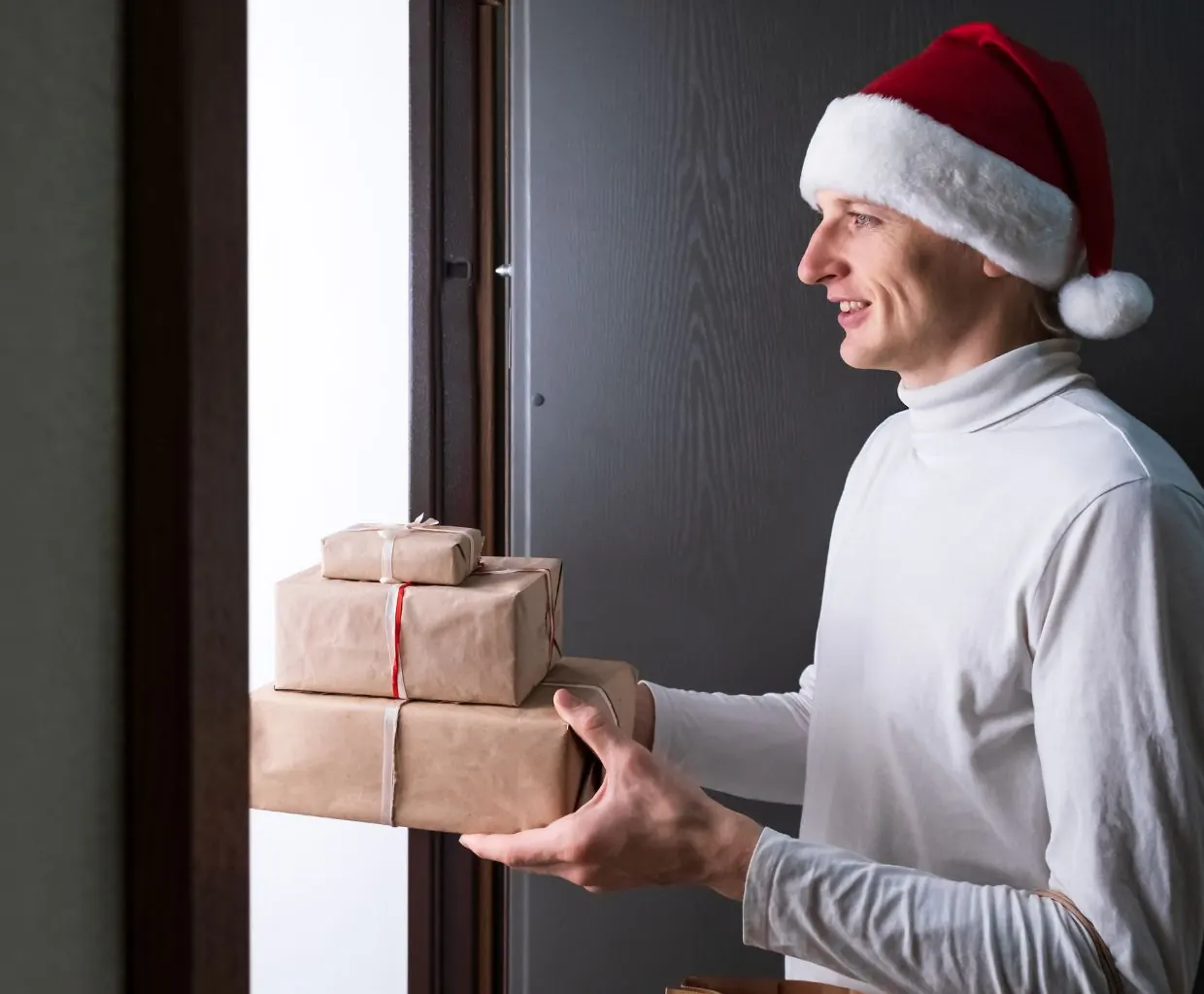 Hombre con gorro de Papá Noel entregando varios regalos envueltos en papel kraft