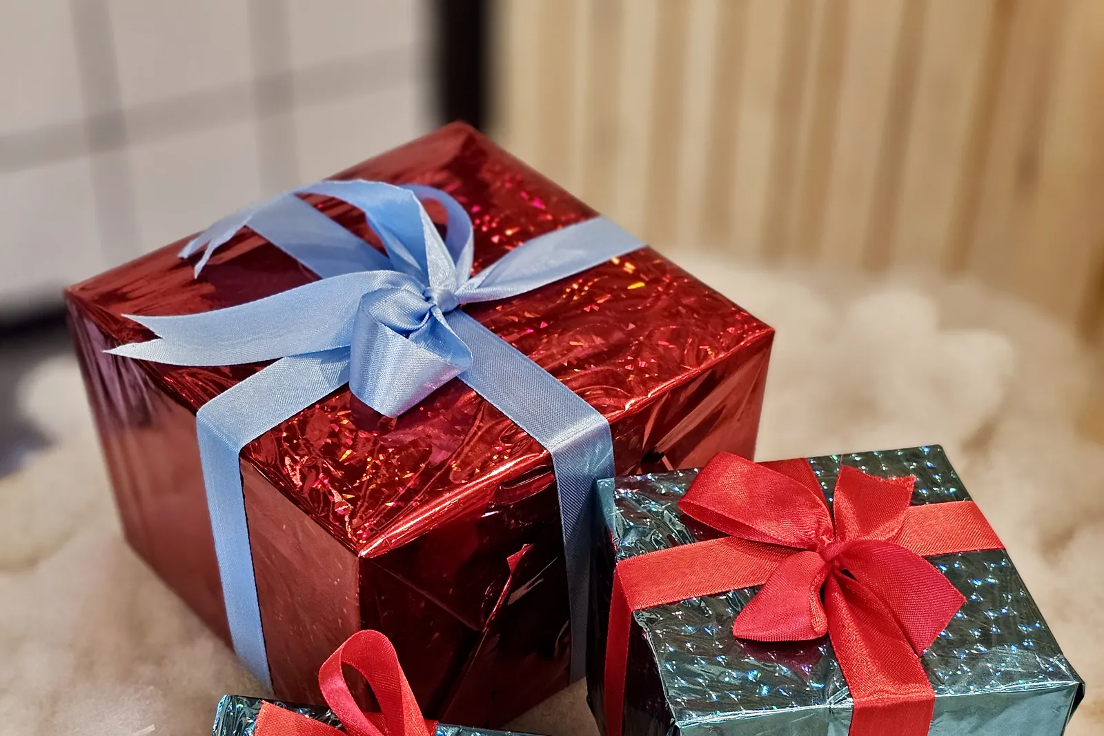 Tres regalos envueltos en papel metalizado rojo y azul con lazos sobre algodón que imita la nieve
