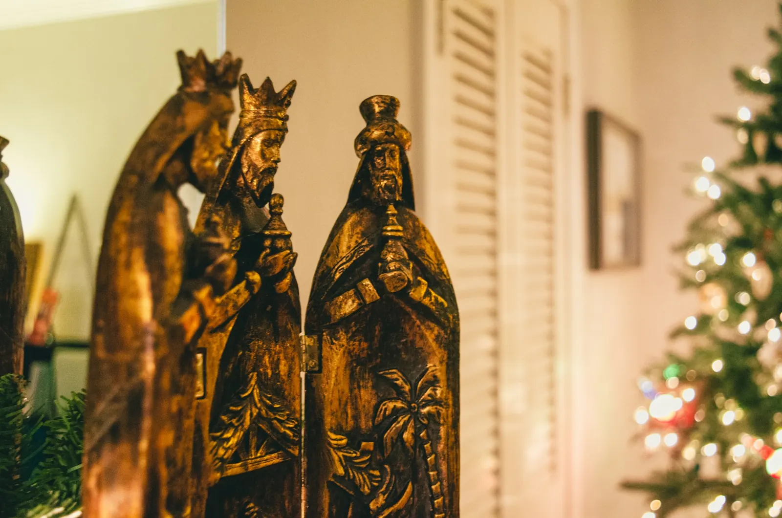 Figuras talladas de los tres Reyes Magos en madera dorada junto a un árbol de Navidad iluminado