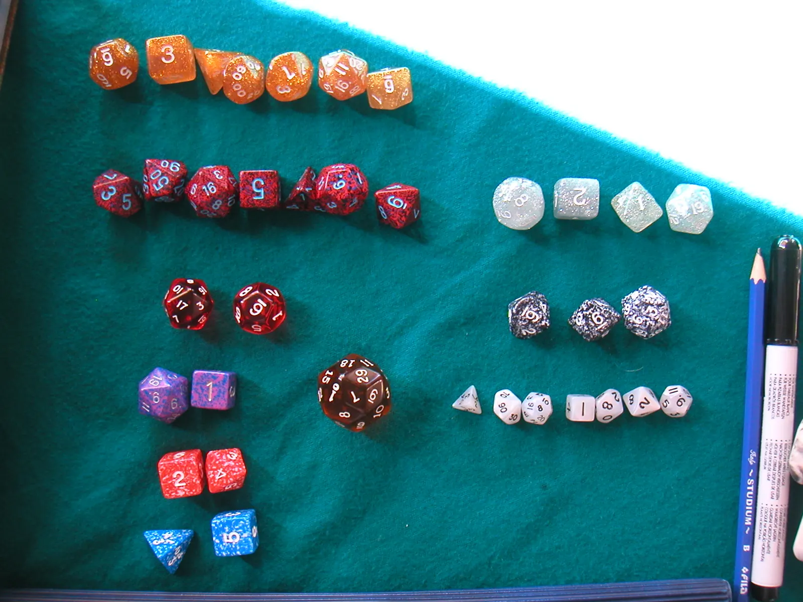 Dados de rol de colores, de cuatro a treinta caras, ordenados en filas sobre un tapete verde