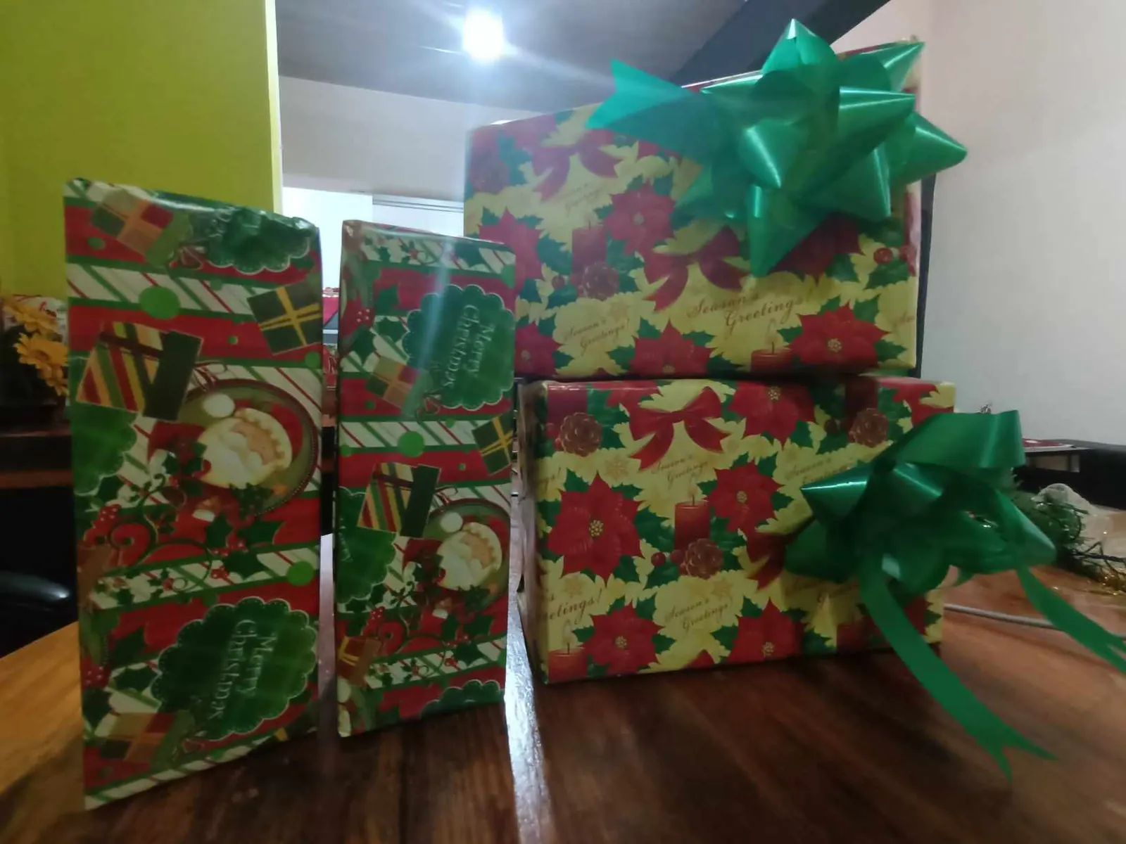 Cuatro regalos envueltos en papel navideño con flores de Pascua y lazos verdes sobre una mesa de madera