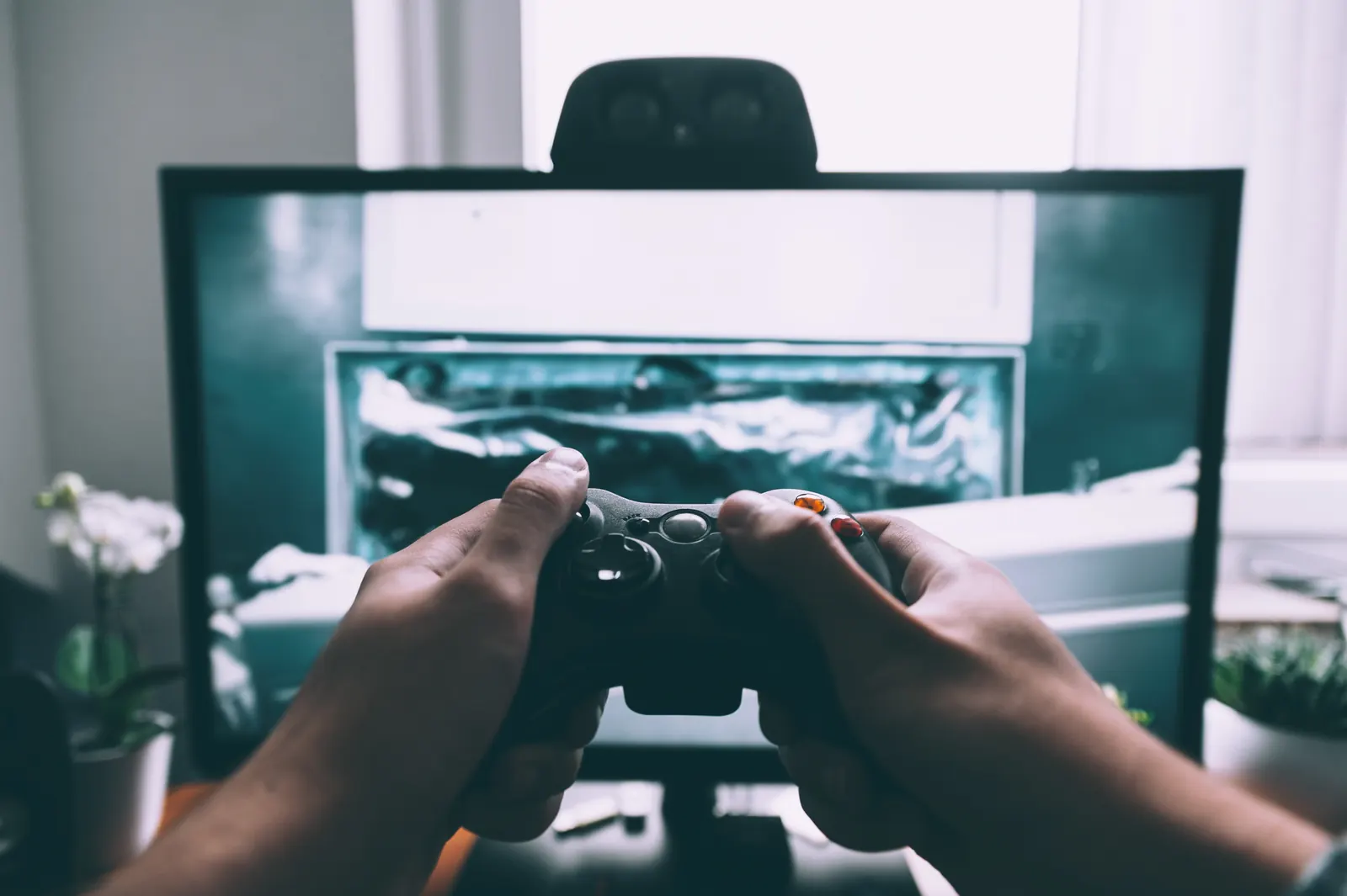 Manos sujetando un mando de videojuegos frente a un monitor con un juego en pantalla