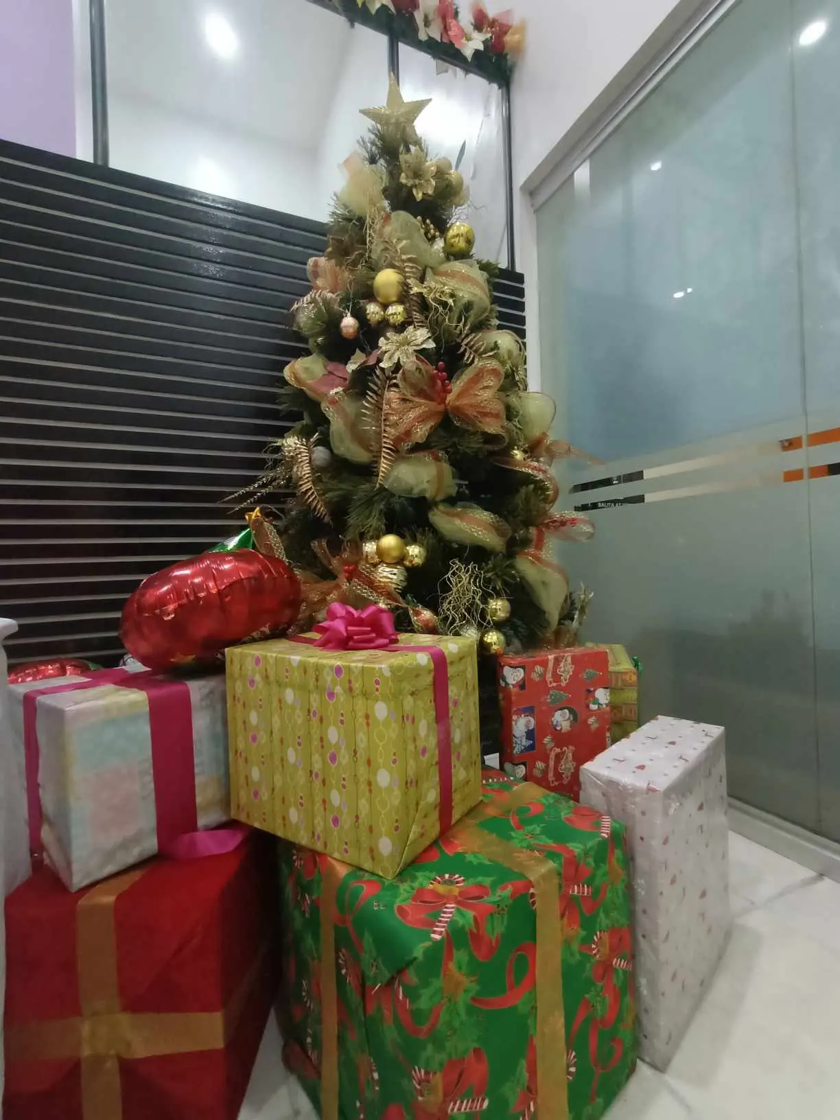 Regalos envueltos en papel de colores con lazos, apilados junto a un pequeño árbol de Navidad decorado en dorado