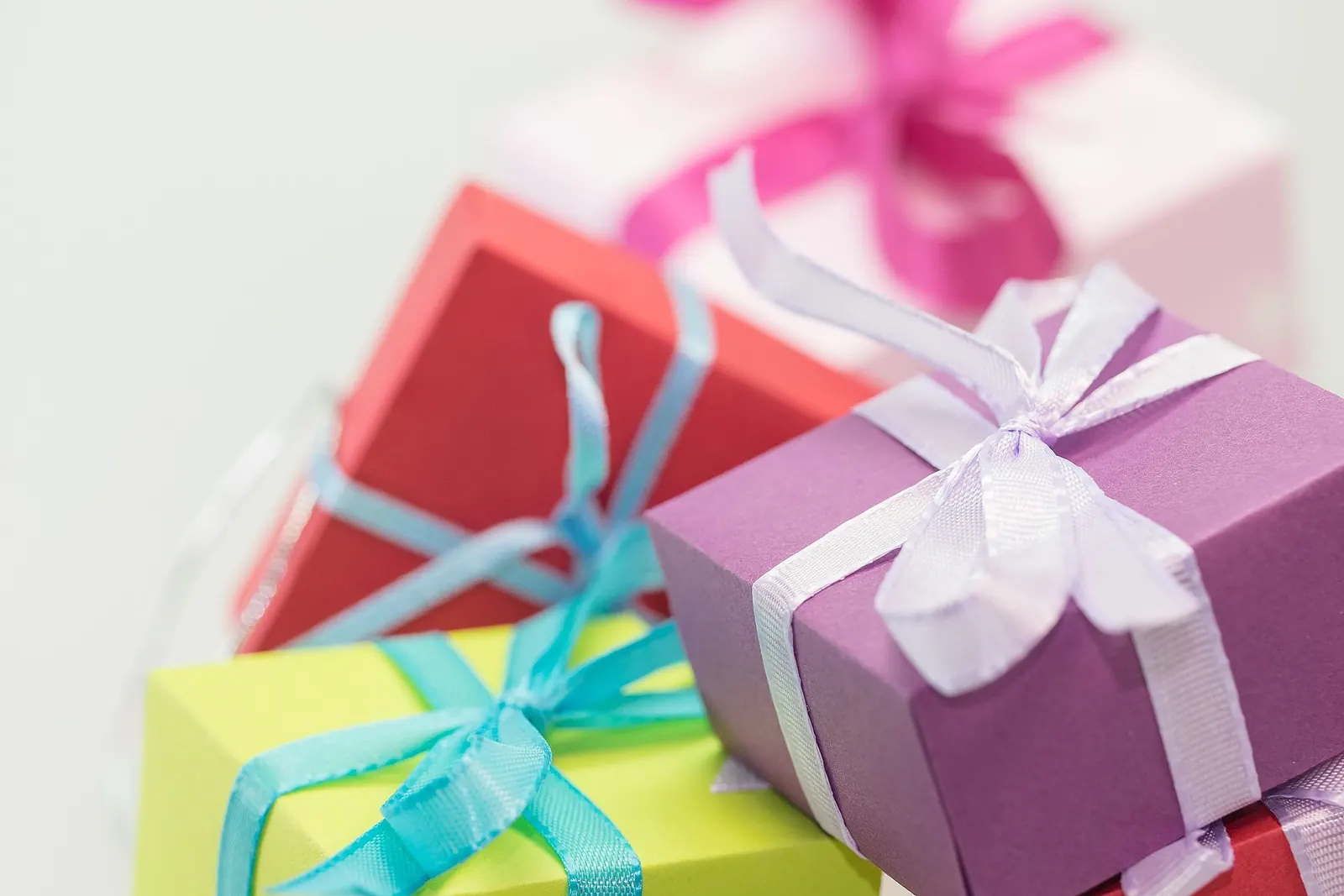 Cajas de regalo de colores, verde, rojo, morado y rosa, atadas con lazos de cinta azul, lila y fucsia
