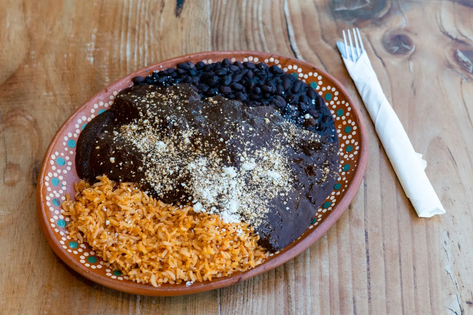 Plato de barro con mole, arroz rojo y frijoles negros sobre una mesa de madera
