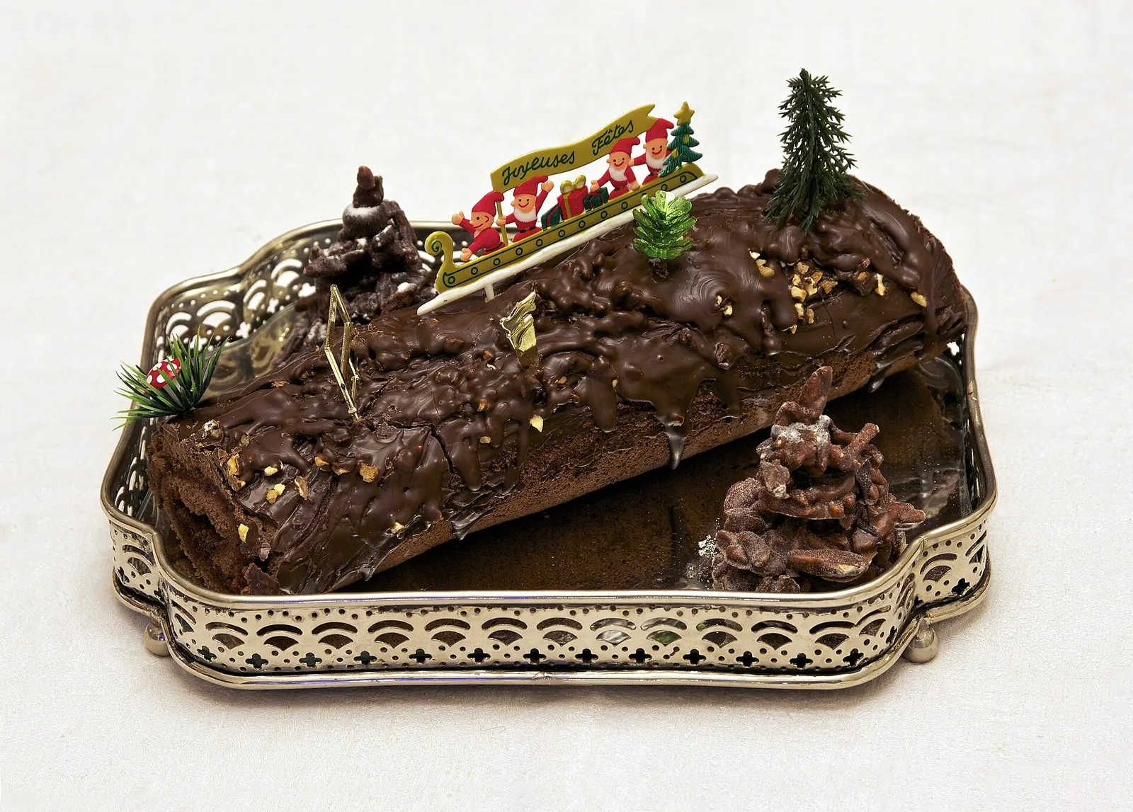 Tronco de Navidad casero de chocolate en una bandeja plateada, decorado con un abeto y figuritas navideñas