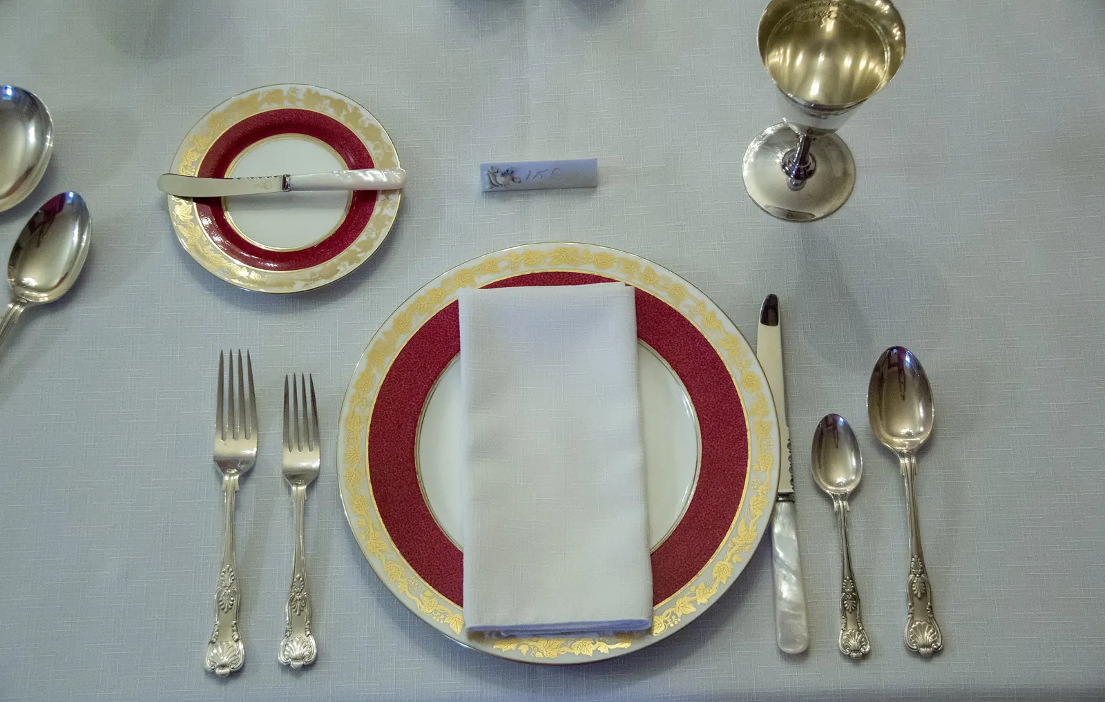 Cubierto de Navidad visto desde arriba: plato con borde rojo y dorado, servilleta blanca, cubiertos de plata y copa